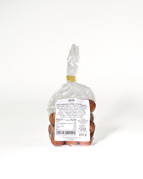Clear Lemke bag filled with marzipan potatoes with a few pieces placed in front. One cut piece shows the pale marzipan center inside the golden brown cocoa coating.