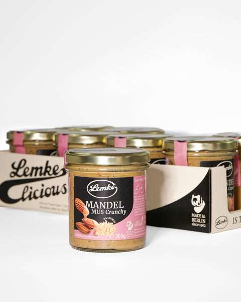 Lemke Mandelmus Crunchy 300 g Glas vor mehreren Gläsern im Displaykarton