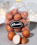 Clear Lemke bag filled with round marzipan potatoes on a grey surface. One cut piece in front shows the pale marzipan center inside the golden brown cocoa coating.