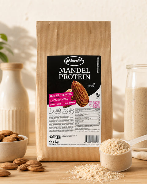 Lemke Mandel Protein 1 kg standing on a wooden countertop in a bright kitchen with whole almonds, a scoop of almond protein powder, and a natural baking setup.