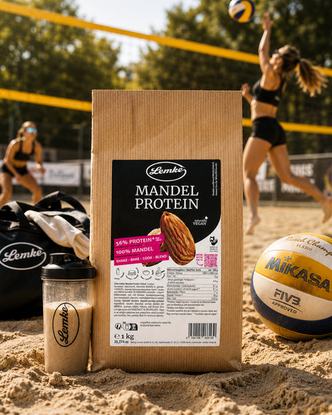 Lemke Mandel Protein 1 kg on a beach volleyball court with a protein shake, sports bag, and volleyball, highlighting plant-based protein for active lifestyles.