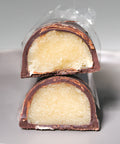 Two cut pieces of chocolate covered marzipan stacked on a white plate. The cross section shows pale almond marzipan inside a dark chocolate shell.