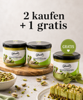 Promotional product image showing three jars of Lemke Stadtstreicher Pistazie pistachio spread on a light background, with two jars on a wooden board and one gift jar with a green ribbon and “Gratis” badge, surrounded by pistachios and a pistachio dessert, plus the headline “2 kaufen + 1 gratis.”