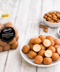 Lemke Marzipan Kartoffel-Konfekt Zimt bag beside a plate of cinnamon marzipan potato sweets, almonds, and cocoa powder on a white wooden tabletop.