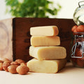 Ein Stapel von Lemke Marzipan Rohmasse Blöcken neben einem Glas voller Marzipankartoffeln und losen Mandeln. Ein Hauch von frischem Grün im Hintergrund rundet das Bild ab.
